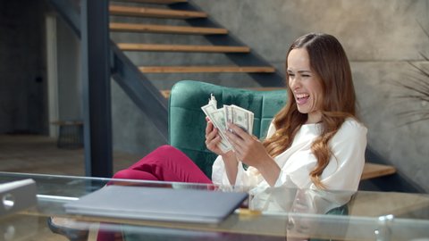 Joyful girl counting money cash in modern office. Successful businesswoman getting bundle of money in office. Happy business woman throwing cash money away in slow motion. Lady hitting jackpot
