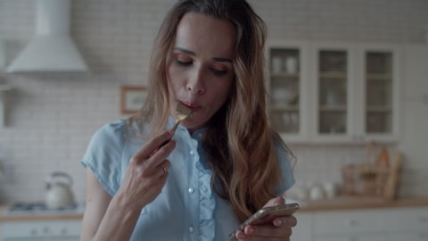 Closeup business woman having lunch in modern kitchen. Attractive lady checking message on phone during lunch at home. Portrait of goodlooking girl eating salad in kitchen in slow motion.