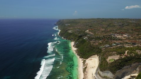 Aerial drone flight over beautiful south coast of island, Bali, Indonesia, 4k. Sunny warm day, water in the indian ocean is deep blue and bright green near shore, small waves near beach with clean