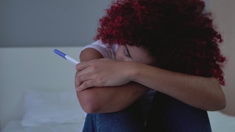 Female teenager holding positive pregnancy test in hand, crying, birth control