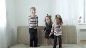 Two baby sister and brother laughing and jumping on sofa at home, slow motion video