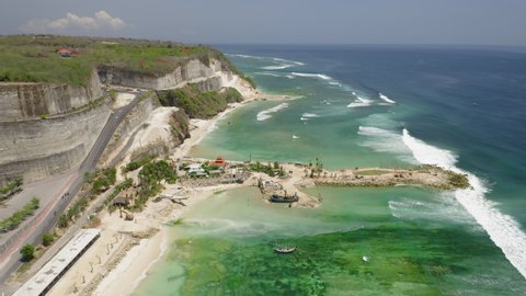 Aerial drone flight over land tonge at Melasti beach, Bali, Indonesia, 4k. New sand spit with constuction site of some buildings. Fantastic view at indian ocean. At sunny day water looks emerald green