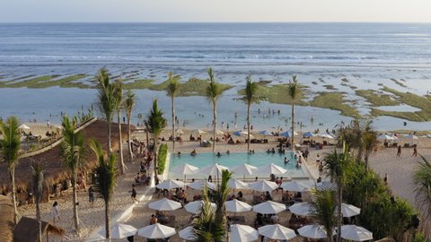 Aerial drone flight over luxury beach club with restaurant, dj music and panoramic swimming pool at Melasti beach, Bali, Indonesia, 4k, december 2019. People are chilling at hot sunny day, having fun