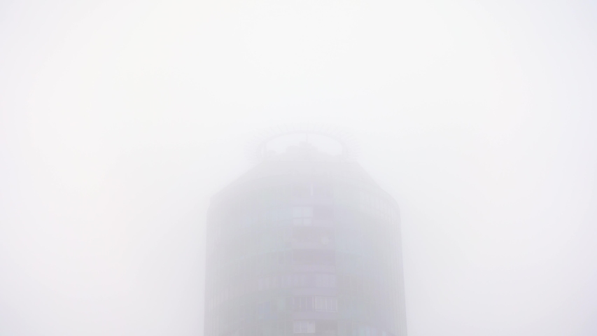 4k Moving shot from top to bottom. Dangerous smog covering silhouette of skyscraper with blue sky. Beautiful view to very dense morning fog over city. 