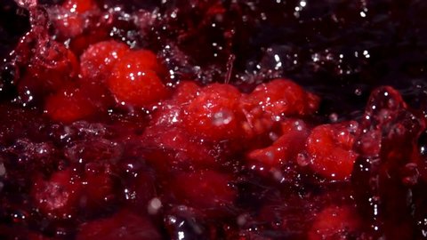 Ripe red delicious raspberries fall into juice with beautiful splashes in slow motion