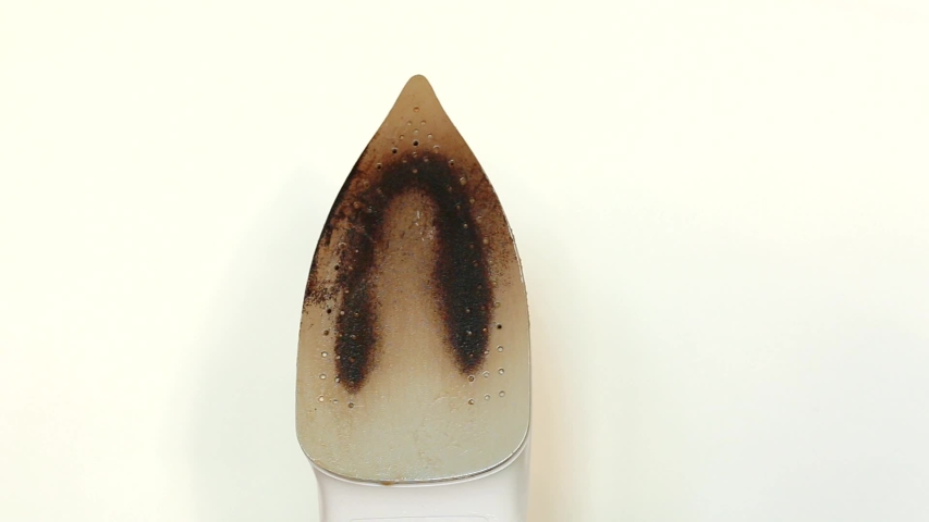 Female hands in yellow gloves sponge the dirty surface of the iron