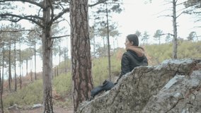 Girl sits on rock in the forest, resting and drinking hot coffee. 4K video