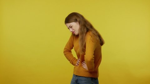 Depressed young woman rubbing painful belly. frowning suffering stomach ache, menstrual cramps in abdomen, constipation and digestion problems. indoor studio shot isolated on yellow background.