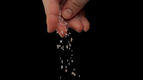 Closeup slow motion of hand of chef cooking food and adding white coarse salt to dish against black background