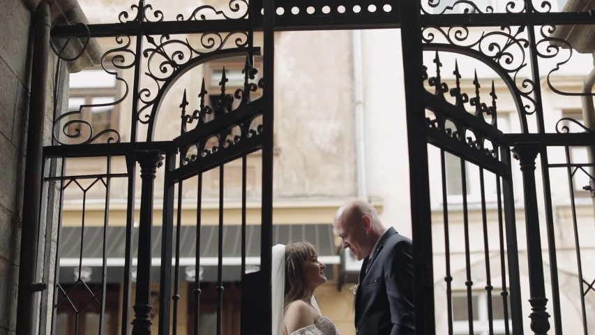 Newlyweds at the old gate making a kiss. Lovely young caucasian bride and groom. Wedding couple. Happy family. Man and woman in love. Slow motion