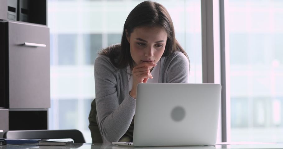 Smiling young woman leaning over table, looking at computer screen, reading email. Pleasant millennial businesswoman typing response to client, working remotely on laptop online alone at office. Royalty-Free Stock Footage #1045279276