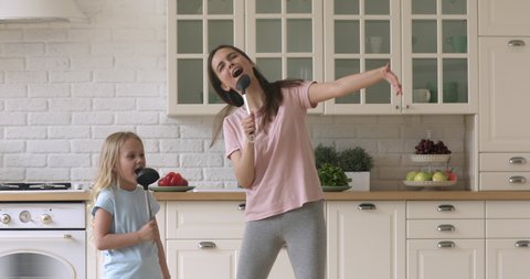 Funny family of two holding ladles, singing favorite song together. Artistic young mommy nanny baby sitter and daughter kid girl having fun, using spoon ladles kitchenware as microphones in kitchen.