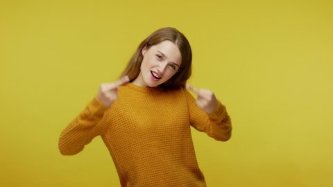 Positive girl in casual pullover showing middle fingers. trying to send off boring asshole with rude gesture and laughing at him, expressing disrespect. studio shot isolated on yellow background