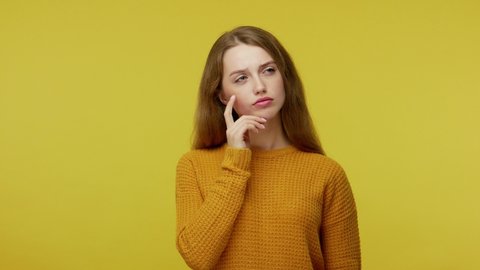 Thoughtful pretty girl with brown hair in pullover rubbing her chin and looking aside with pensive expression. pondering a solution, doubting question. indoor studio shot isolated on yellow background