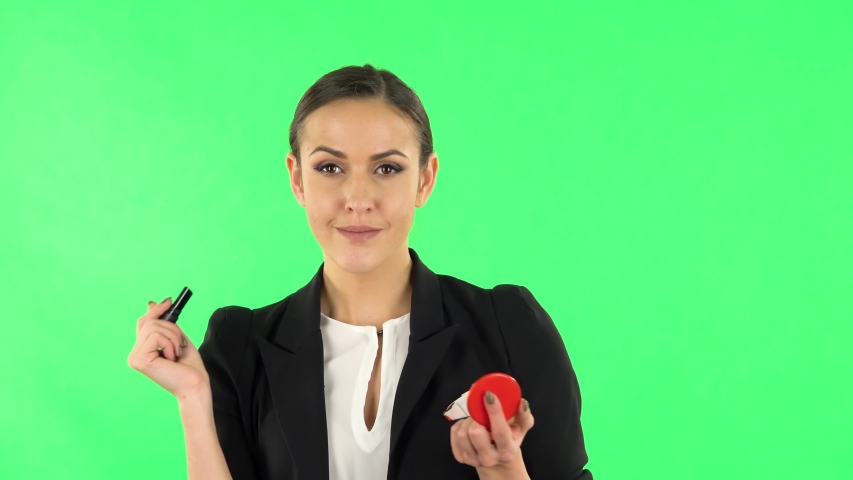 Girl paints her lips looking in red mirror. Green screen