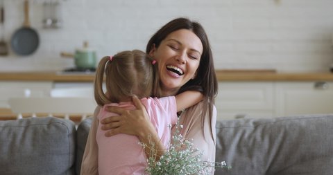 Sincere young mother embracing cuddling little preschool daughter. Happy 30s mom feelings thankful to small kid girl for birthday 8 march international woman s day congratulations, holding flowers.