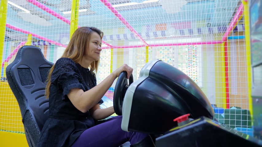 Satisfied young woman smiling while sitting in car driving simulator attraction in children s amusement park