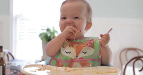 Cute baby eating messy meal of spaghetti, sitting in highchair.