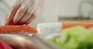 Restaurant kitchen. Male sushi chef prepares Japanese sushi rolls of rice, salmon, avocado and nori. takes a large piece of fish and puts it on sushi