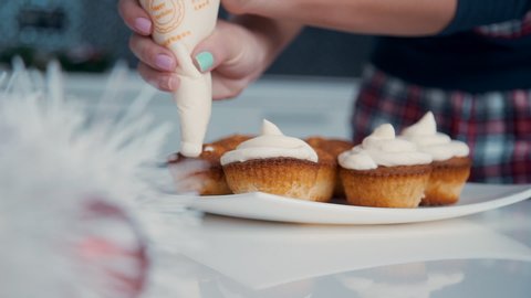 Decorating cupcake with white cream. Using cooking bag, confectioner make muffins for party. Shot of woman's hands putting butter cream on the tasty cakes, homemade bakery