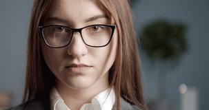 Portrait of attractive young woman with brown eyes looking at camera and adjusting eyeglasses. Professional businesswoman in formal wear standing at modern office.