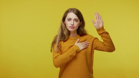 I swear! Responsible girl with sincere face expression raising hand to take oath, promising to be honest and to tell truth, keeping hand on chest. indoor studio shot isolated on yellow background