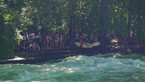 MUNICH, GERMANY – JUNE 2019: Gimbal pan shot left to right of surfers in Surf English Park Munich in summer sunny day. Gimbal shot of surfing in Munich park