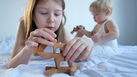 two children. brother and sister are sitting on a white bed and playing wooden toys. safe eco-friendly wooden toys in the form of animals
