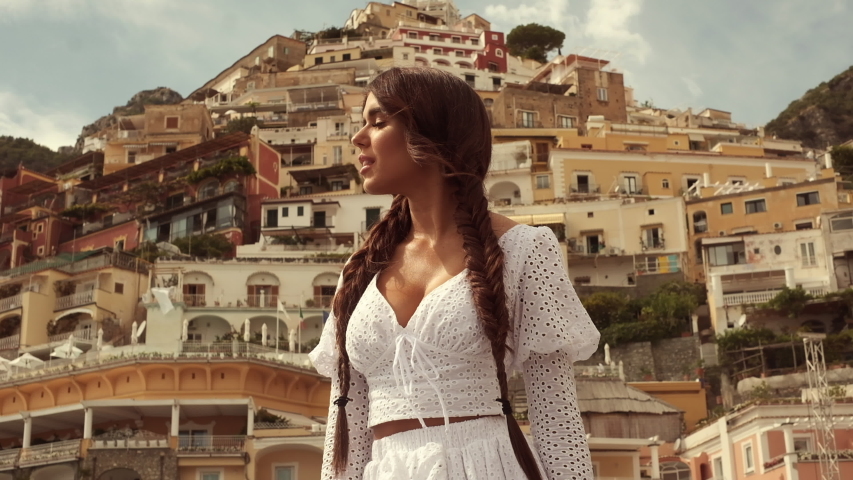 Young Brunette On Background Of Houses On The Hills In Positano. Italy. Girl Looks At The Landscape Hiding Her Face From The Sun.