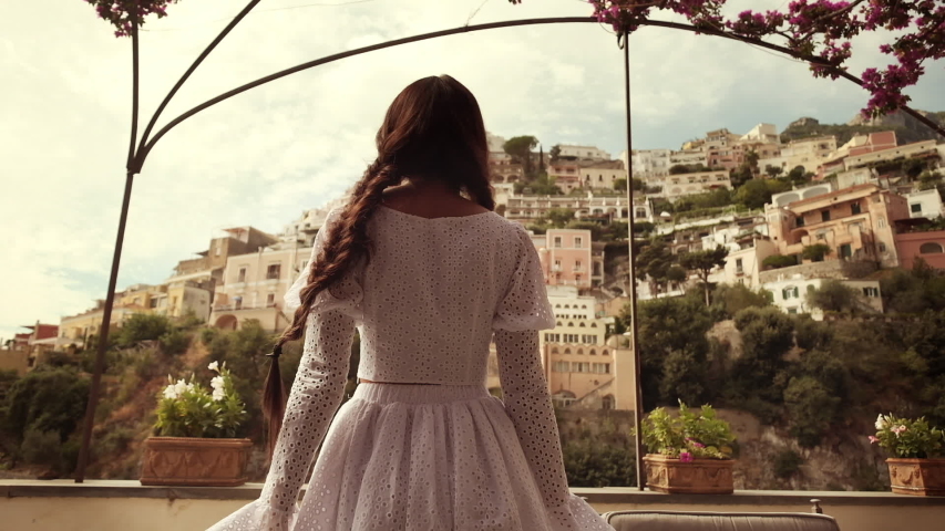 Young Brunette Enjoys The Landscape In Positano. Italy. Girl Looks At The Magnificent Landscape Of The Sea And Houses On The Rocks.