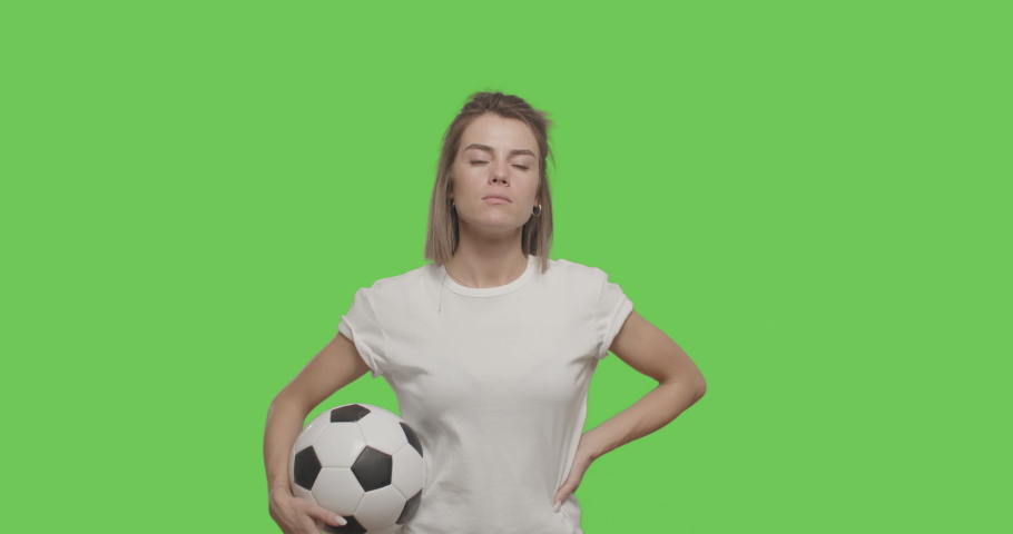 Caucasian girl football player in white t-shirt chewing bubble gum Sporty woman holding ball looking at camera having fun over Green Screen, Chroma Key.  Slow motion 60 fps