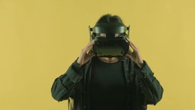 Young woman looks around and wonders how amazing  in the VR world. Virtual reality helmet on the yellow background. Portrait