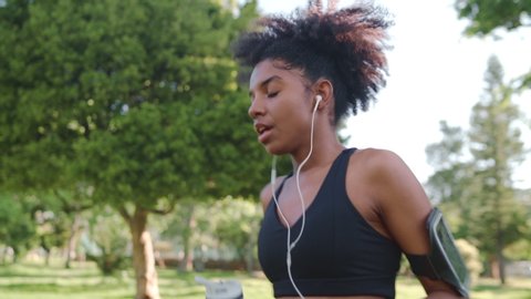 african american Young woman athlete drinking water from reusable bottle and heavily breathing after morning workout in the park