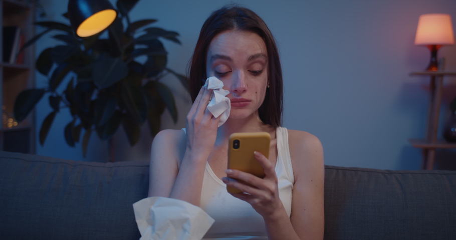 Close up of young woman wiping tears from her face with paper tissue while looking at phone screen. Upset girl cant believe bad news reading on her smartphone and crying. | Shutterstock HD Video #1045403965