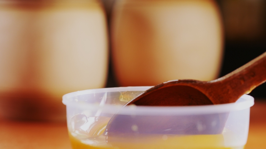 rustic wooden spoon with pouring sweet honey over plastic bowl on table shows natural properties slow motion close view