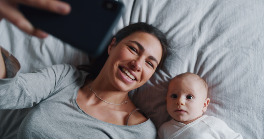 Authentic close up of neo mother and her newborn baby making a selfie or video call to father or relatives in a bed. Shot in 8K. Concept of technology, new generation,family, connection, parenthood | Shutterstock HD Video #1045412311