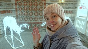 Portrait of a lovely young smiling woman makes a video call or message on the phone, waves and blows a kiss with two illuminated deer in the background. 4K