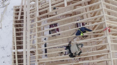 Top ascending aerial view of builder working on the roof of wooden residential frame house under construction 庫存影片