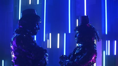 Two dancers a man and a woman standing opposite each other, shaking in time to the music synchronously head in sparkling mirrored costumes in blue violet color of shimmering neon