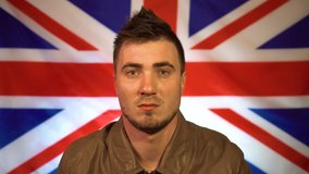 British punk in a leather jacket with a mohawk on his head with a bold expression on his face, looking from side to side and straightening his jacket against the background of the flag of UK
