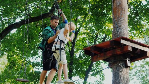 Kharkov, Ukraine, July 2019: Instructor helps child in maze of ropes high in tree branches