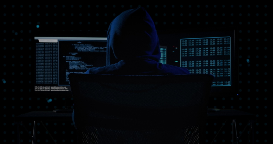 Portrait of mysterious hooded hacker sitting at desk and looking at the camera after breaks into government data servers in dark atmosphere with system codes animation in background. Royalty-Free Stock Footage #1045464274