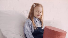 Cheerful kid with gift box on bed