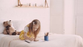 Kid drawing with pencils while sitting on bed