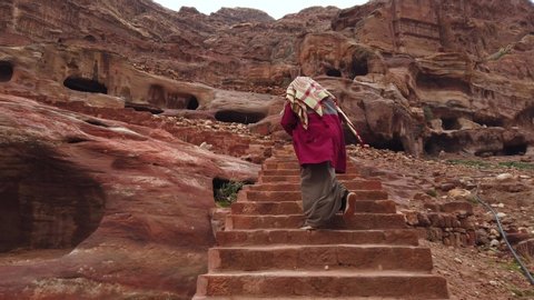 The Bedouin climbs the stairs to Petra. An Arab woman climbs up the steps in the ancient city of Petra. A woman dynamically climbs an old staircase in the rocks of an ancient city.  庫存影片