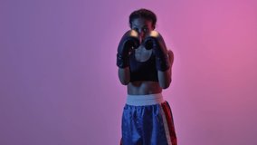Concentrated african sports woman boxer training in boxing gloves while looking at the camera isolated led flashlights background