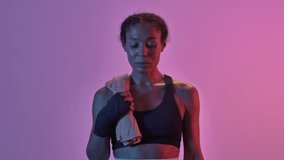 Happy african sports woman boxer standing with towel and looking at the camera isolated led flashlights background