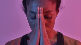 Close up view of concentrated african sports woman praying with pray gesture and looking at the camera isolated led flashlights background