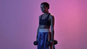Concentrated african sports woman doing exercise with dumbbells isolated led flashlights background
