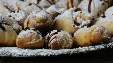 Freshly baked homemade croissants with icing sugar on top poured with chocolate icing on a large plate in the kitchen.